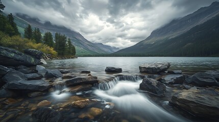 Stream flowing into tranquil mountain lake under dramatic cloudy sky