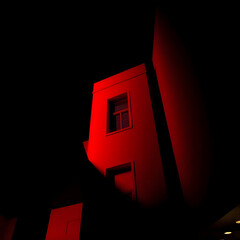 This image features a striking, minimalist architectural detail, showcasing a sharp, angular structure in deep red, likely a building or monument, set against an almost black background. The strong co