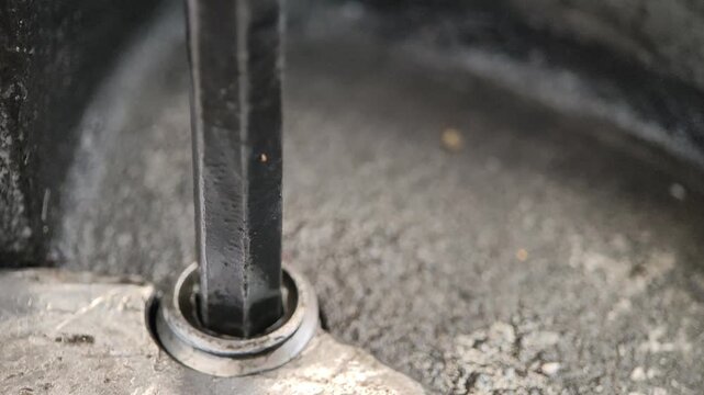Close-up of a metal L-shaped hex key (Allen wrench) being used to tighten or loosen a hex socket bolt in a gritty, industrial, or mechanical assembly, highlighting repair work.