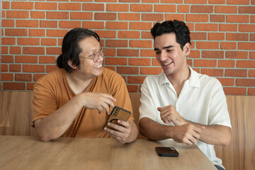 Two men smiling friends chatting casual meeting smartphone coffee shop brick wall wooden table relaxed mood social interaction technology