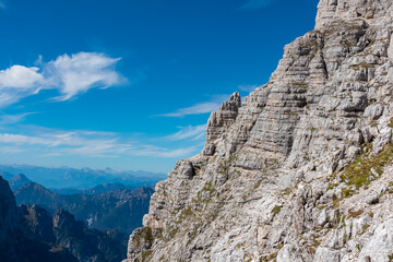 The sheer, stratified limestone face of a majestic mountain looms against a vivid blue sky, showcasing the raw power and geological details of Julian Alps for climbers and adventurers alike in Italy.