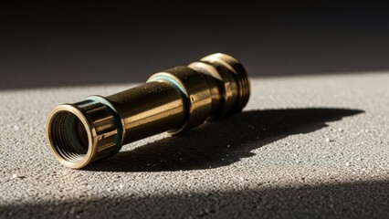 A brass plumbing pipe fitting rests on a textured grey surface casting a sharp shadow in bright sunlight