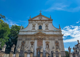 Obraz premium Magnificent Baroque facade of the Church of St. Peter and St. Paul stands behind statues of twelve apostles. This stunning religious landmark in Krakow is viewed from below against a clear blue sky.