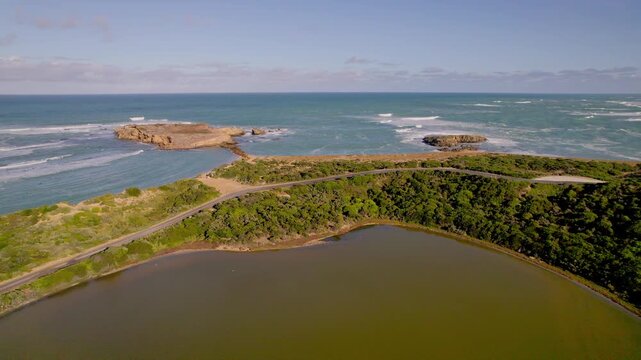 Backward aerial flight over Siloam Pool in Beachport, showing the yellowish water, the rugged coastline, and Post Office Rock. The wide coastal scenery creates a bright, scenic and natural atmosphere.