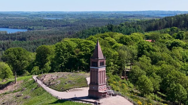 Aerial footage of the Himmelbjerget sky tower standing tall on a hilltop surrounded by lush green forest and distant views.