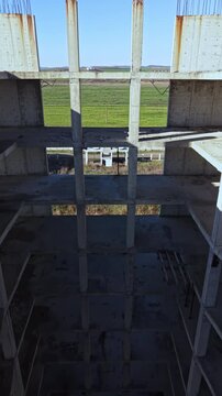 An unfinished construction site reveals a vast vertical shaft surrounded by tall concrete columns. Sunlight illuminates the deep cavity, highlighting scattered debris.