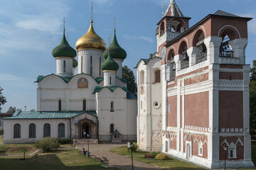 Historic white stone cathedral with golden and green domes alongside a red brick bell tower in Suzdal, Russia.