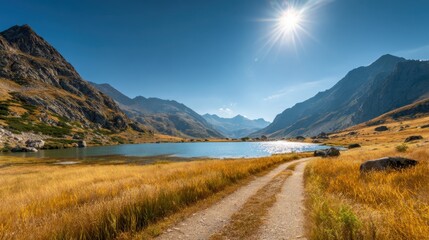A serene mountain scene features a calm lake surrounded by grassy fields and rocky terrain. The sun shines brightly illuminating the stunning landscape in the afternoon light.