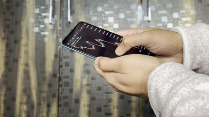 Close up of trader hand holding smartphone, using trading app with stock market charts for financial analysis and monitoring investment data. - Powered by Adobe