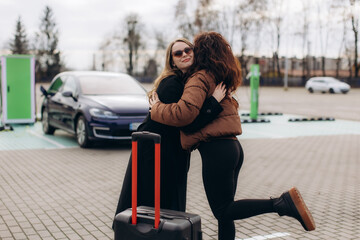 Women friends embracing at electric car charging station