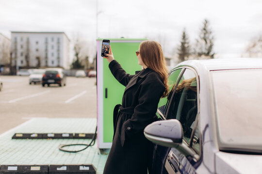 Woman taking selfie at electric car charging station - Powered by Adobe