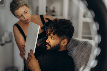 Woman cosmetologist applying permanent makeup to man eyebrows