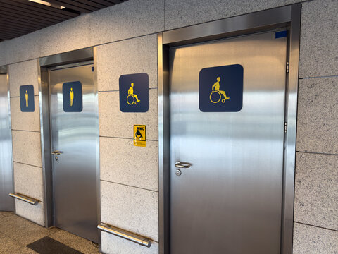 Entrance door to accessible restroom next to men restroom features wheelchair and gender symbols. Wheelchair accessible restroom with universal icons. WC for handicapped person with Braille text