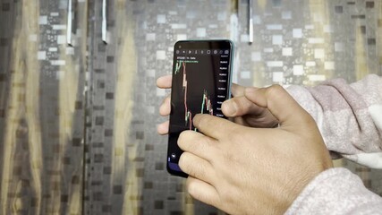 Close up of trader hand holding smartphone, using trading app with stock market charts for financial analysis and monitoring investment data. - Powered by Adobe
