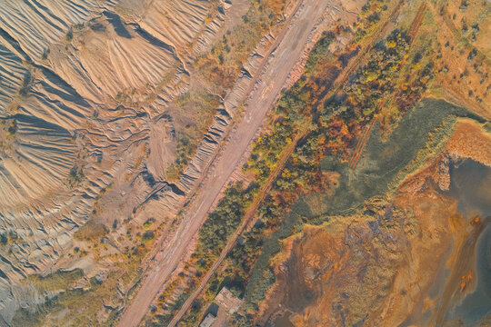 Aerial abstract composition showing industrial damage. Eroded quarry walls contrast with a geometric road and autumnal vegetation, illustrating technogenic pollution and land degradation.