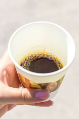 Paper cup of black coffee held in hand outdoors, close-up drink shot.
