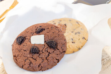 Two large soft cookies with chocolate chips on white paper close-up. High quality photo
