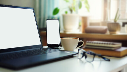 close up shot, office desk with laptop, mobile phone, coffee cup, eyeglasses and notebook placed on table by the window and sunlight