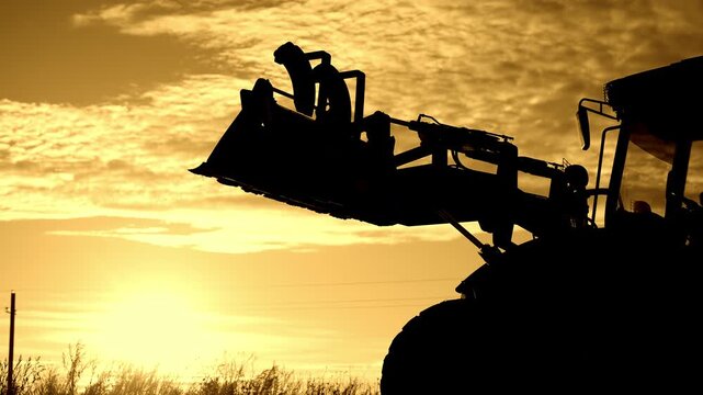 Silhouette of moving tractor, earthworks and digging ground in construction site . Professional operating contemporary building or agricultural machinery, farming or processing soil in farm or ranch