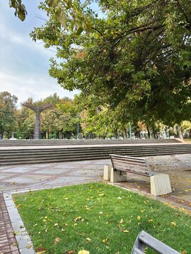 Park bench, grass, and steps leading to a sculpture on an autumn day