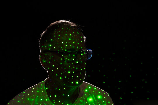 Man with glasses covered in green dots of light on black background