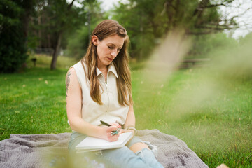 Woman journaling in notebook on blanket in green park