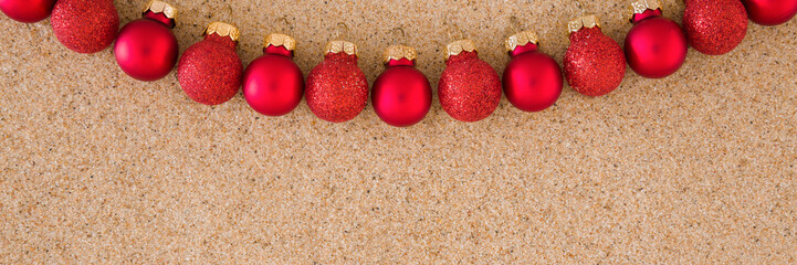 Beautiful shiny red baubles on light brown dry sea sand background. Closeup. Christmas decoration....