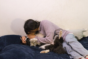 Woman on a bed in home clothes hugs and kisses a black and white dog. Scene of affection and relaxation, suitable for pet care, friendship, or cozy lifestyle projects.