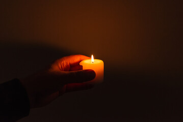 Burning candle in the mans hands on a dark background. Religious concept. Selective focus. Side...