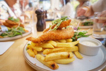 Fish and chips on a plate. Unrecognizable people dining in the restaurant. Auckland.