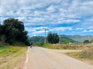 Distant Cyclist on Paved Road with Mountain View and Clear Sky