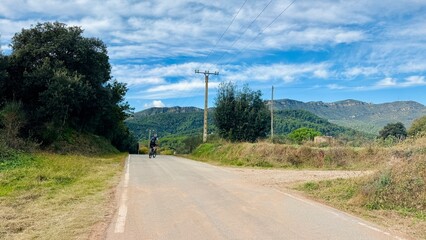 Distant Cyclist on Paved Road with Mountain View and Clear Sky