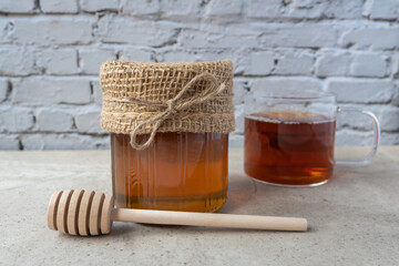 Glass bowl of natural honey, cup of tee and wood spoon on the table.