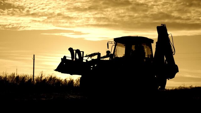 Worker working on bulldozer, backlit silhouette of powerful building machinery. Beautiful sunset or sunrise in countryside, professional dozer driver or famer, earthworks and engineering works