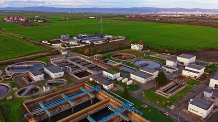 Beneath a vibrant sky, a wastewater treatment facility operates diligently among expansive green fields. The landscape reflects technology and nature working together harmoniously.
