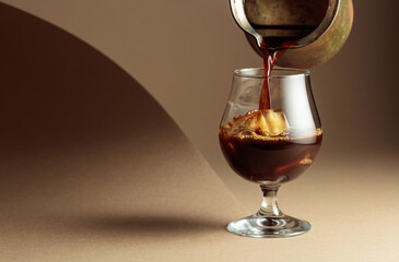 Black coffee is poured into a glass with ice.