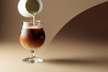 Cream is poured into a glass with iced coffee.