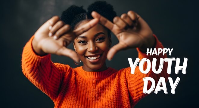 A smiling young Black woman in an orange sweater frames her face with her hands, celebrating Youth Day. - Powered by Adobe