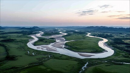 An aerial view of a wide, winding river flowing through a lush green valley. The landscape features rolling hills in the distance and a soft, pastel sky at dusk