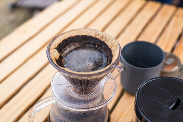 A close-up of manual pour over coffee brewing on an outdoor wooden table, showing the filter and coffee grounds.
