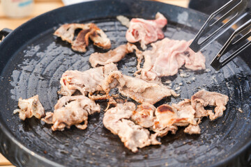 Sliced meat being grilled on a hot pan, indicating a process of preparing a savory meal.