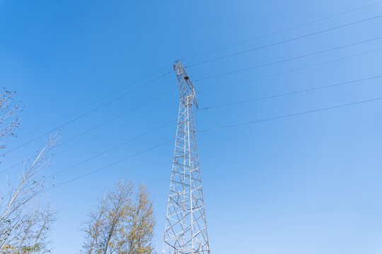 A high voltage power transmission tower with multiple cables against a clear blue sky, showcasing industrial infrastructure. - Powered by Adobe
