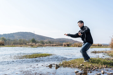 Fototapeta premium A man is practicing martial arts by the river in an open air environment, showing a dynamic stance.