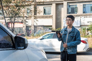 A man is using a high pressure water gun to wash a car outdoors on a sunny day.