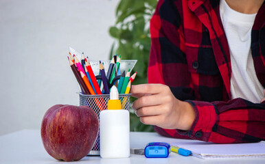 Smart young boy in glasses preparing for school, choosing pencils from the organizer on his desk.