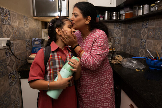 A mother gives an affectionate kiss to her daughter before she heads out with her school bottle