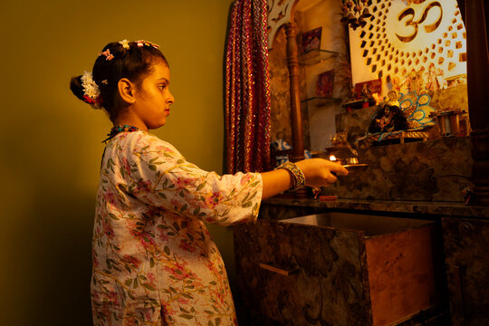 A young girl performs aarti at the home temple with focus and devotion