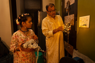 A man untangles decorative lights while his daughter watches and helps with the decorations