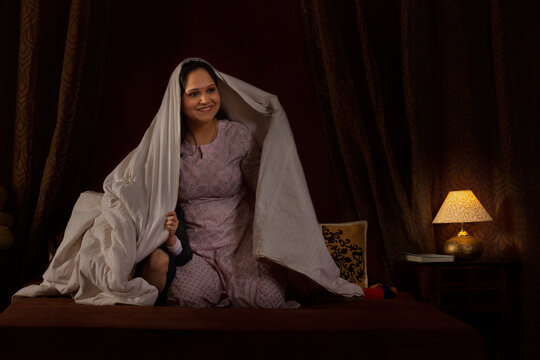 Happy mother playing with her two little kids with blanket on bed