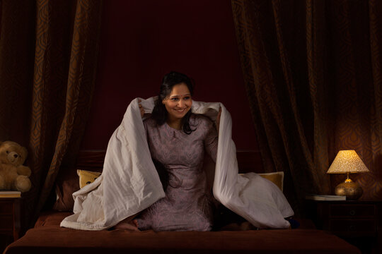 Happy mother playing with her two little kids with blanket on bed
